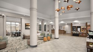 A spacious lobby with high ceilings, large columns, a seating area with sofas and tables, and a reception desk with a display of items. - Hilton Garden Inn Dallas Lewisville (Lewisville)