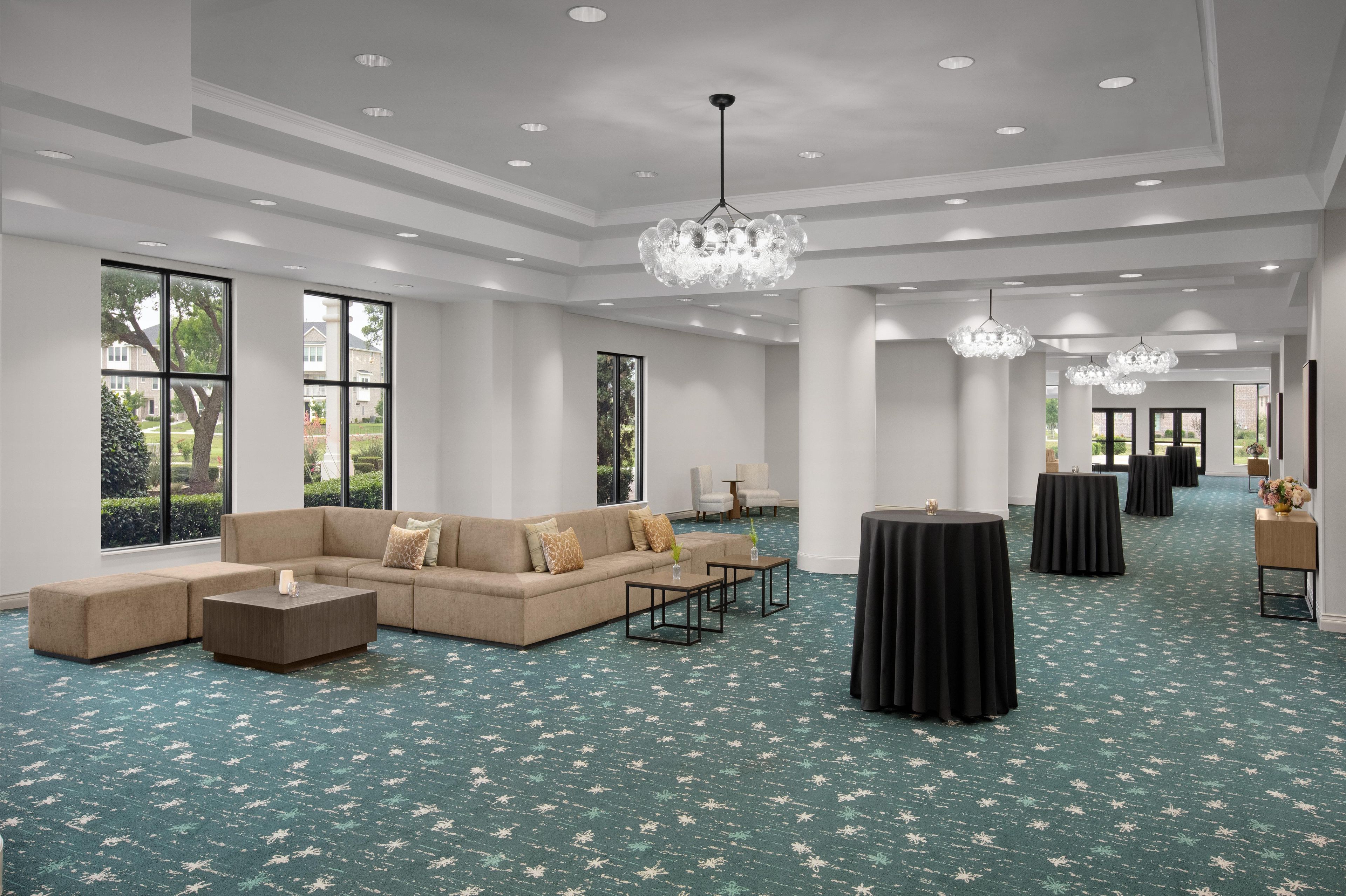 A spacious hotel lobby with a large sectional sofa, multiple tables, and a chandelier.