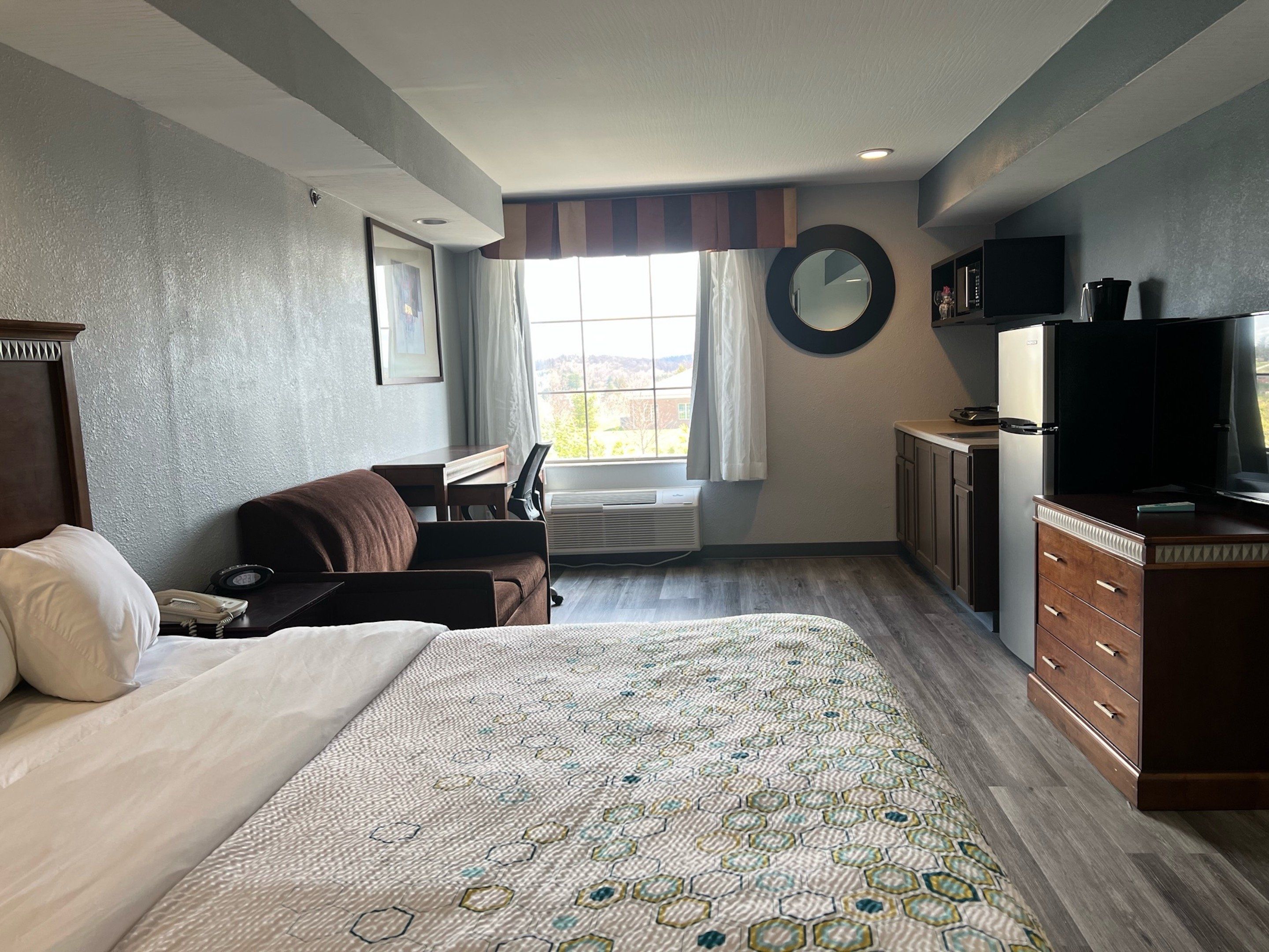 A hotel room with a large bed, a desk, a chair, a TV, and a window with curtains.
