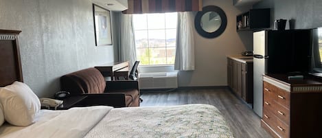 Habitación de hotel con una cama grande, un escritorio, una silla, un televisor y una ventana con cortinas.