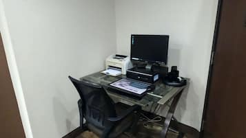 Oficina en esquina con escritorio, computadora, impresora y un reloj en la pared.