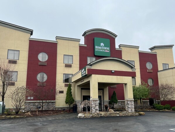 A multi-story hotel with a red and beige facade, a sign for 'HomeTowne Studios', and a stone facade entrance. - HomeTowne Studios & Suites By Red Roof Washington (Washington)