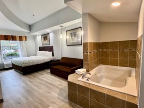 A modern hotel room with a large bed, a sitting area, a bathtub, and a window with a view of the outside. - HomeTowne Studios & Suites By Red Roof Washington (Washington)
