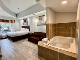 Habitación de hotel moderna con una cama grande, un área de descanso, una bañera y una ventana con vistas al exterior.