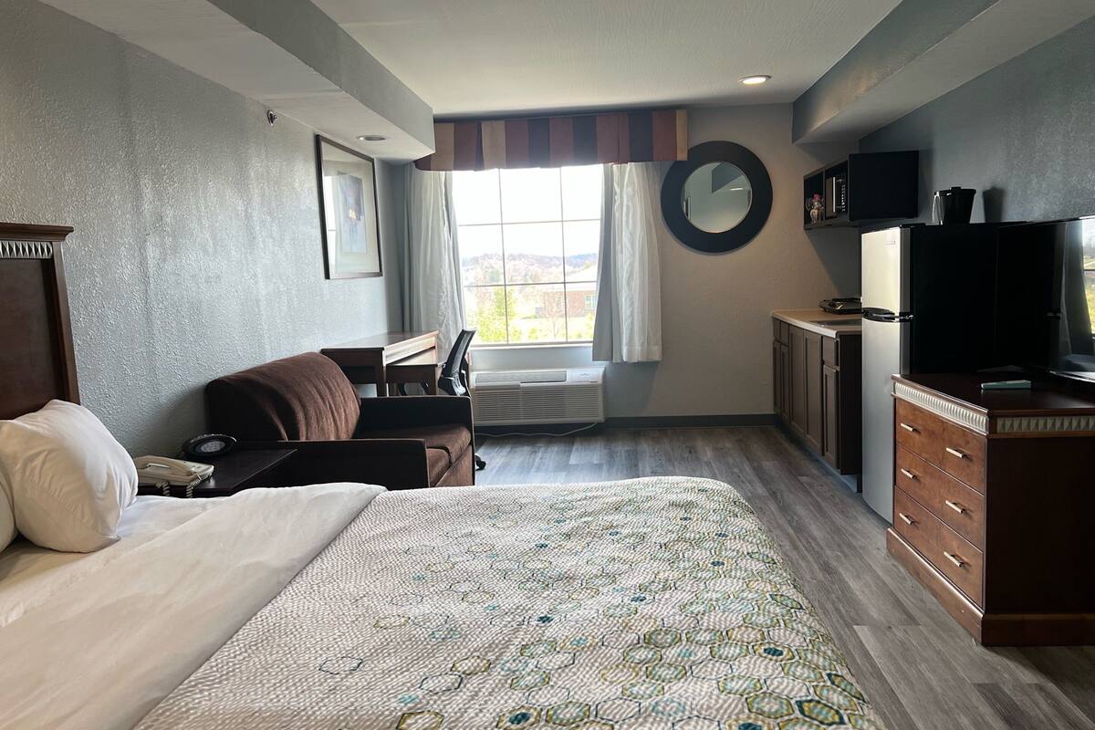Quarto de hotel com uma cama grande, uma escrivaninha, uma cadeira, uma televisão e uma janela com cortinas.