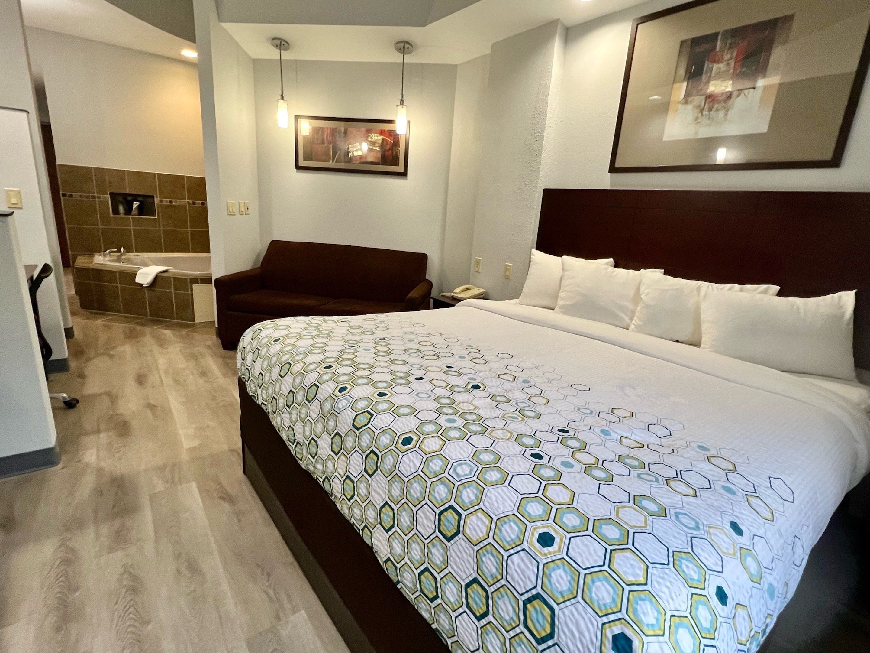 Une chambre d’hôtel avec un grand lit, un canapé, une baignoire et un tableau encadré au mur.