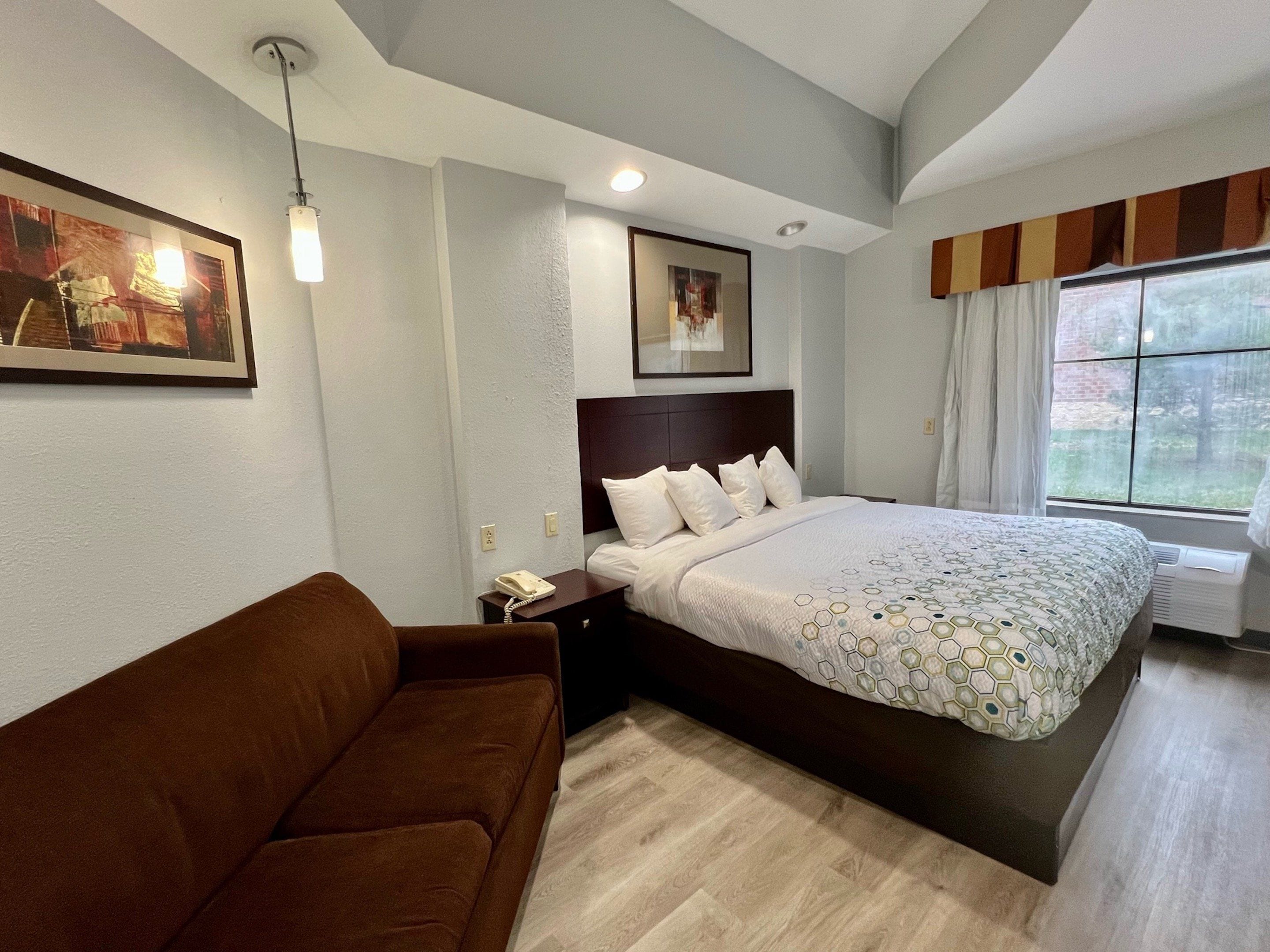 A hotel room with a large bed, a brown sofa, a telephone, and artwork on the walls.