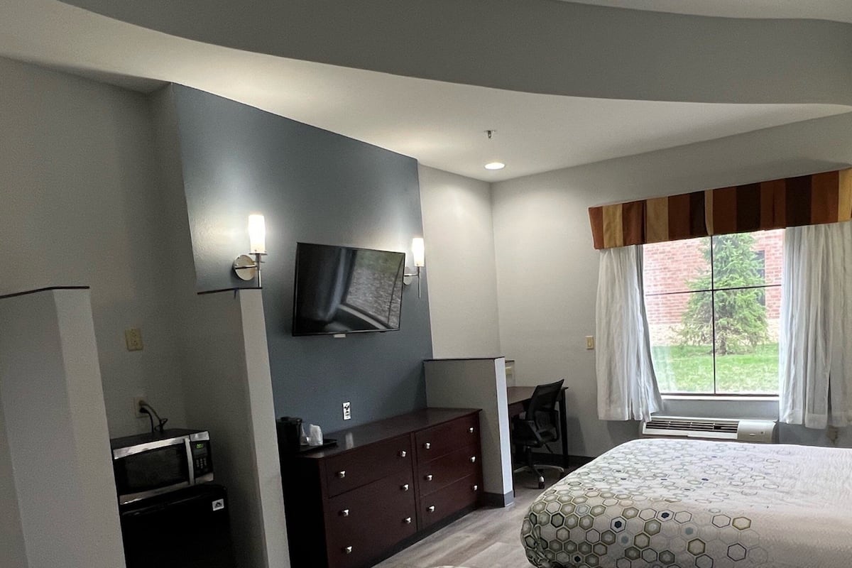 Quarto com cama, cômoda, televisão e janela com cortinas.