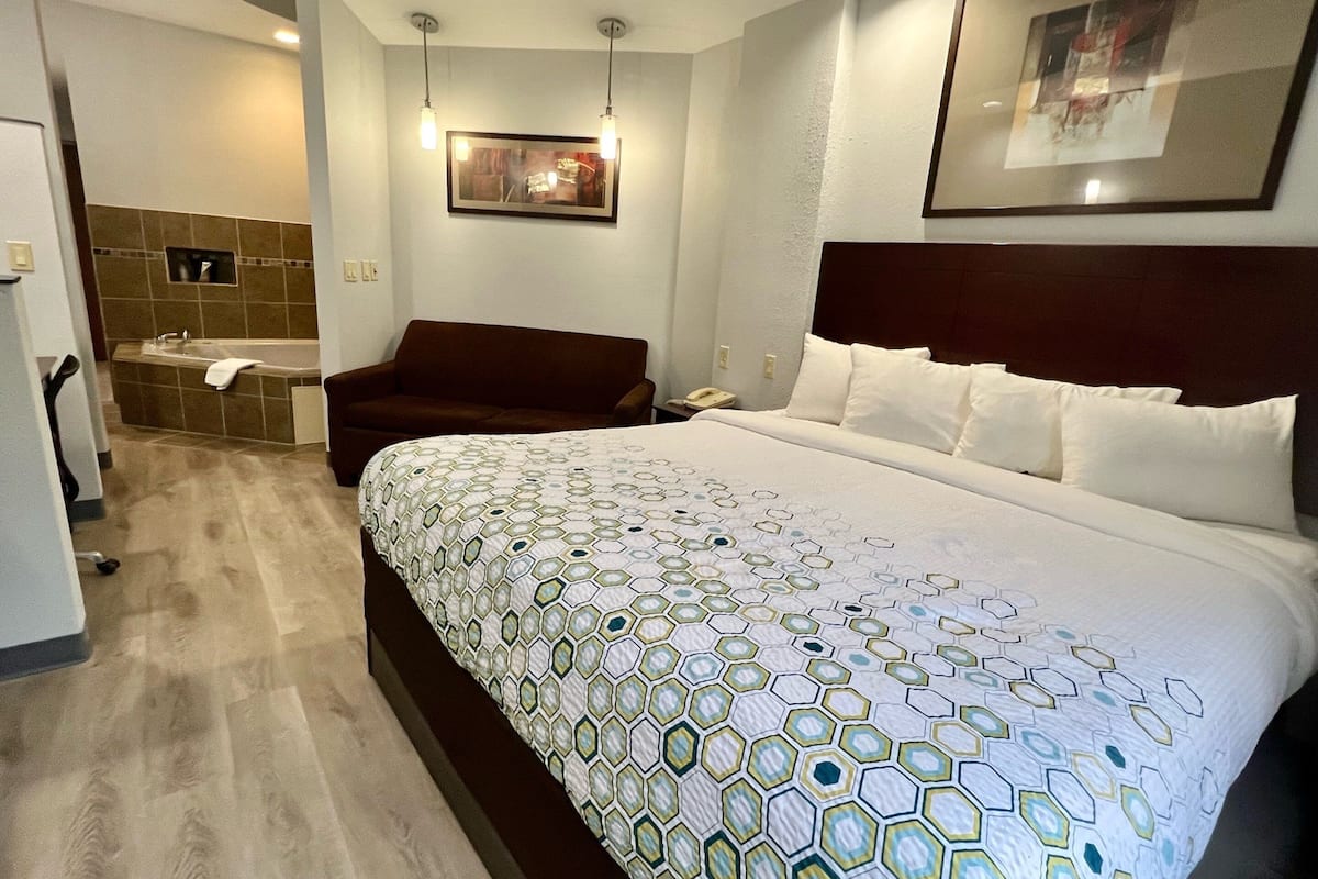 Quarto de hotel com uma cama grande, um sofá, uma banheira e um quadro na parede.