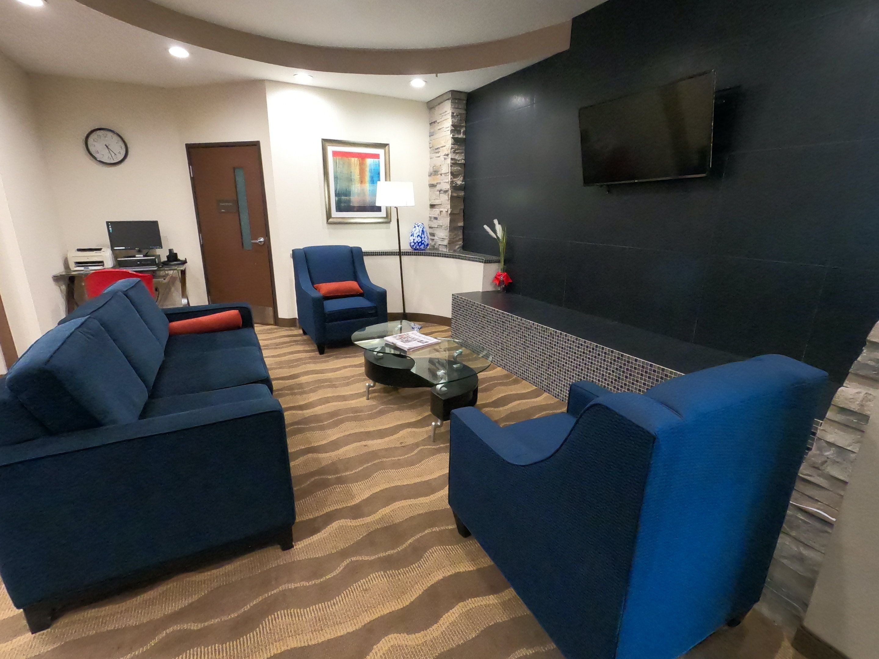 A modern living room with blue sofas, a glass coffee table, a fireplace, and a flat-screen TV mounted on the wall.