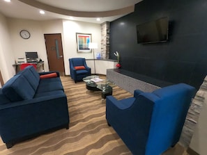A modern living room with blue sofas, a glass coffee table, a fireplace, and a flat-screen TV mounted on the wall. - HomeTowne Studios & Suites By Red Roof Washington (Washington)