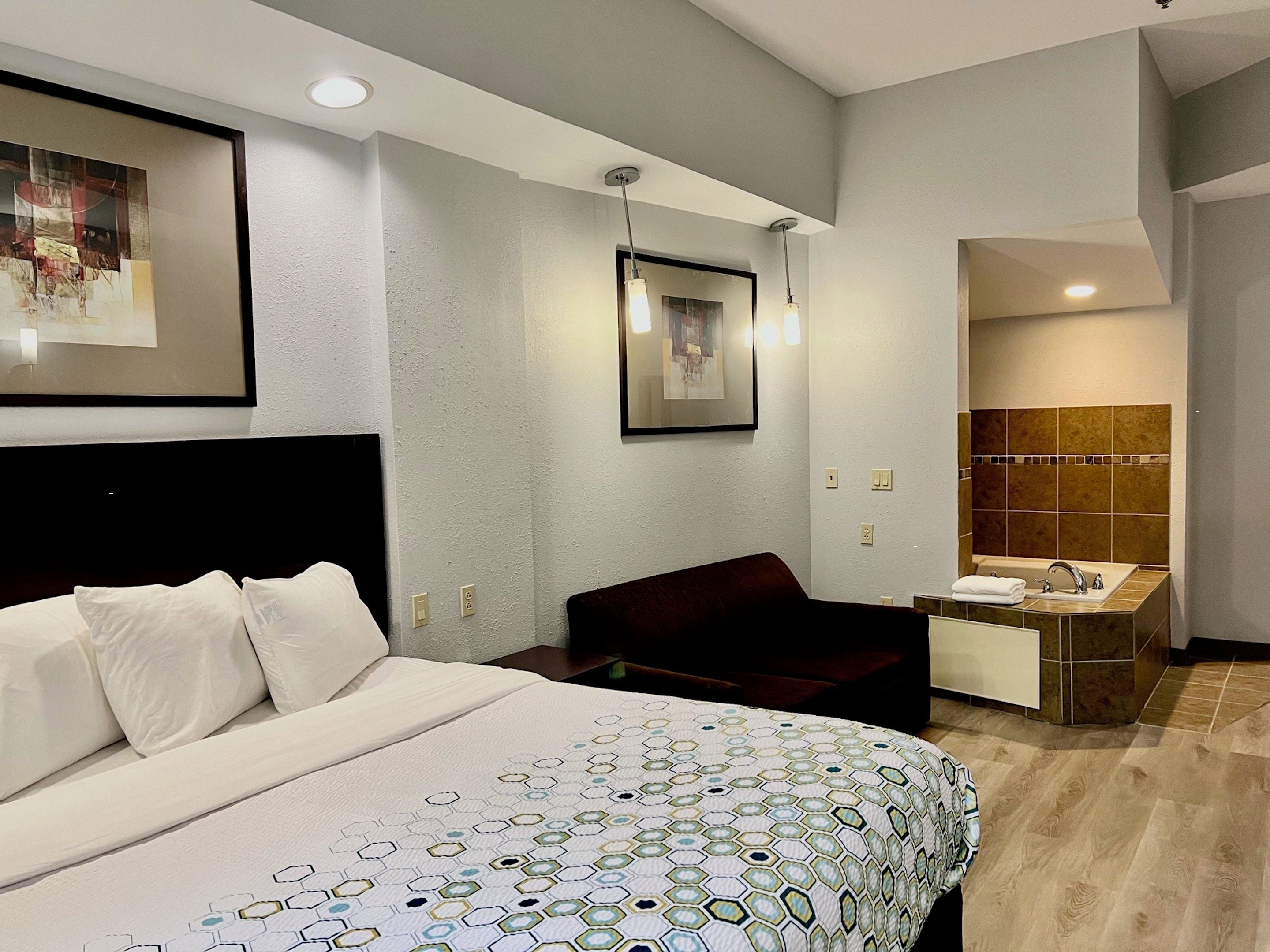 Habitación de hotel con cama, escritorio, silla, baño con lavamanos y espejo, y obras de arte en las paredes.