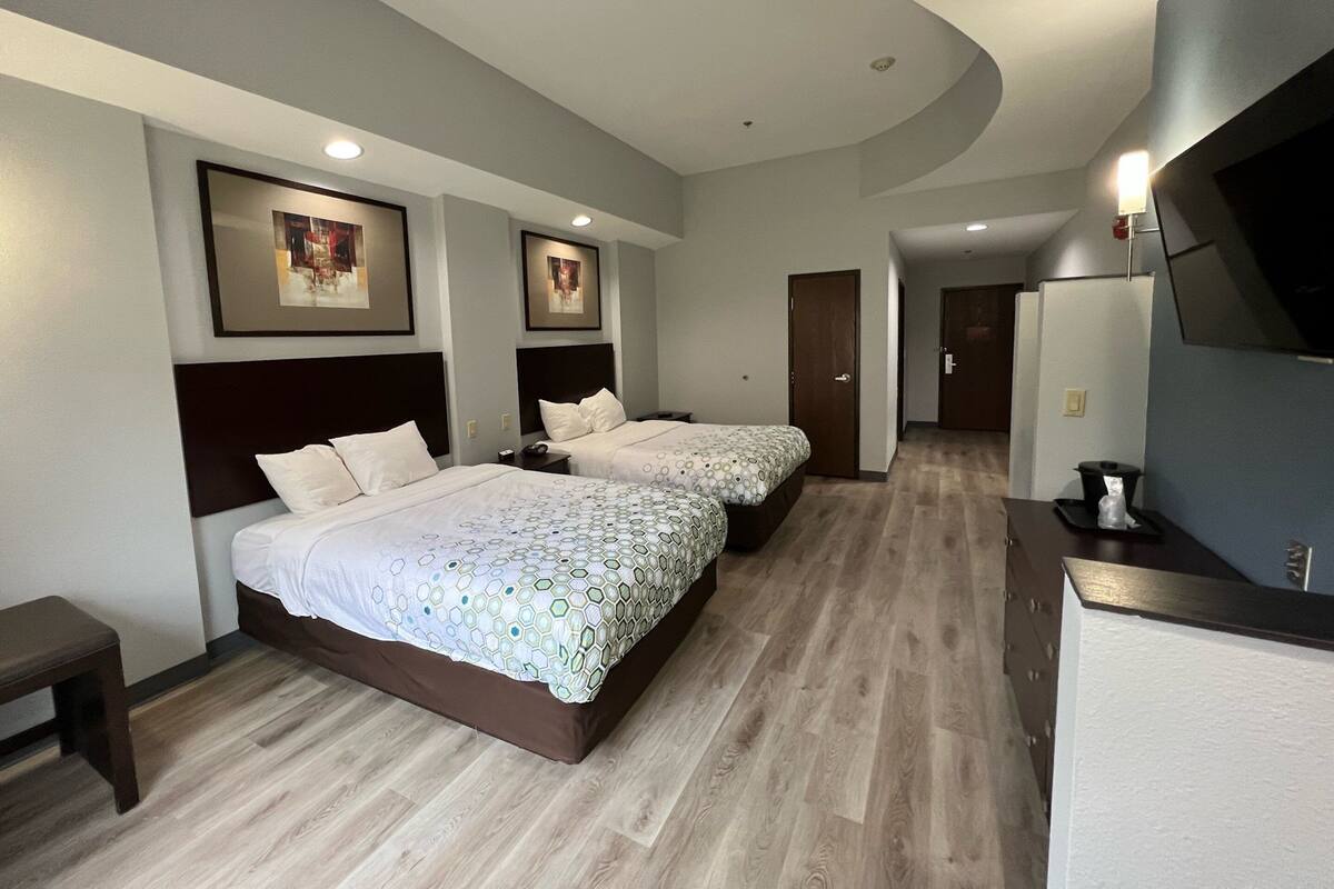 Quarto de hotel com duas camas, uma mesa, uma televisão e um banheiro.