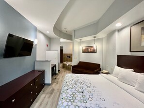 A hotel room with a bed, a TV, a desk, a chair, and a sofa. - HomeTowne Studios & Suites By Red Roof Washington (Washington)