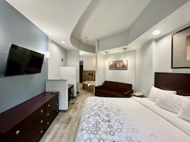 Quarto de hotel com cama, televisão, escrivaninha, poltrona e sofá.