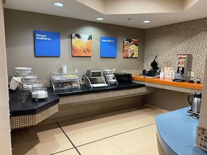 A breakfast area with a buffet setup, including a coffee machine, a microwave, and various food items. - HomeTowne Studios & Suites By Red Roof Washington (Washington)