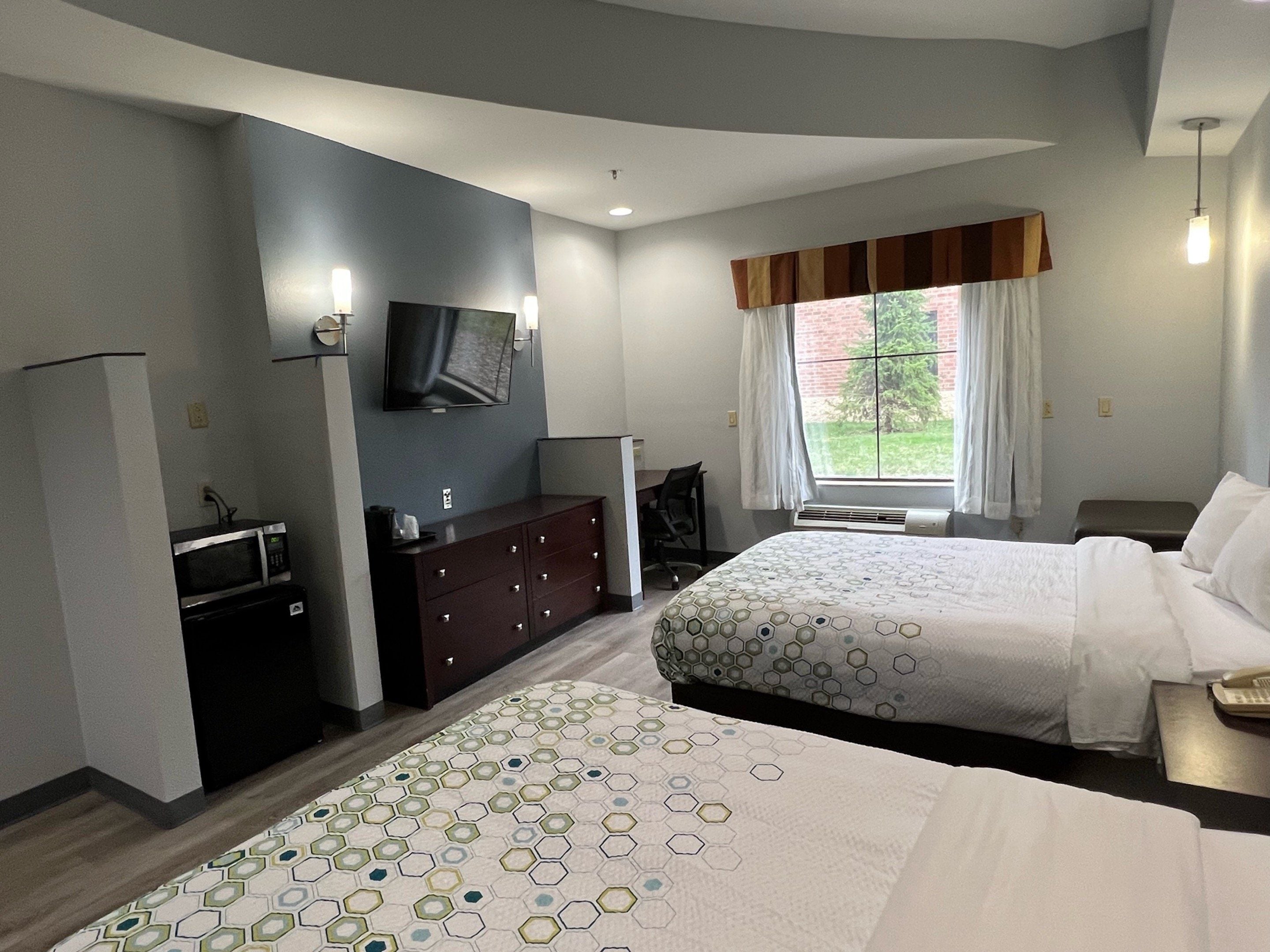 A hotel room with two beds, a desk, a TV, and a window with curtains.