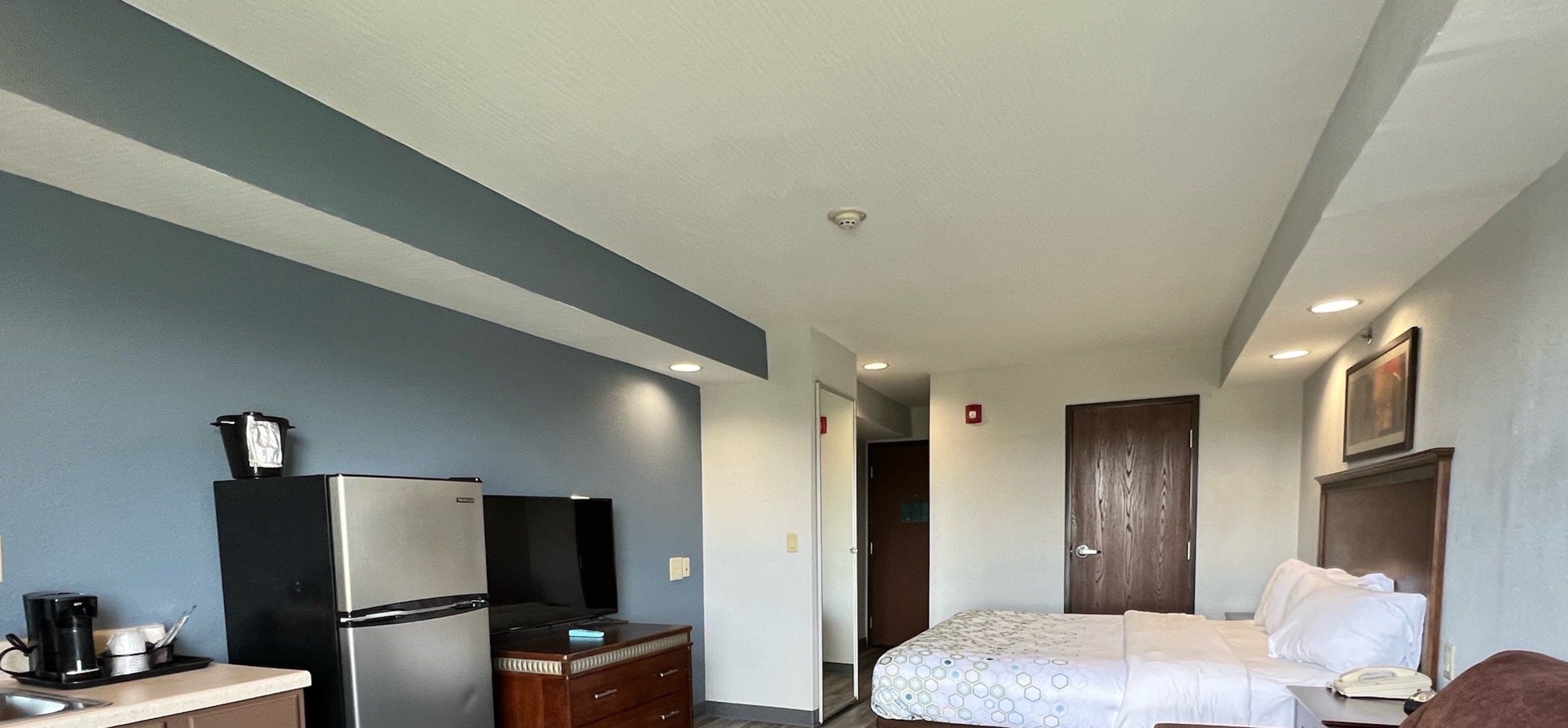 A hotel room with a kitchenette, a bed, a desk, and a wardrobe.