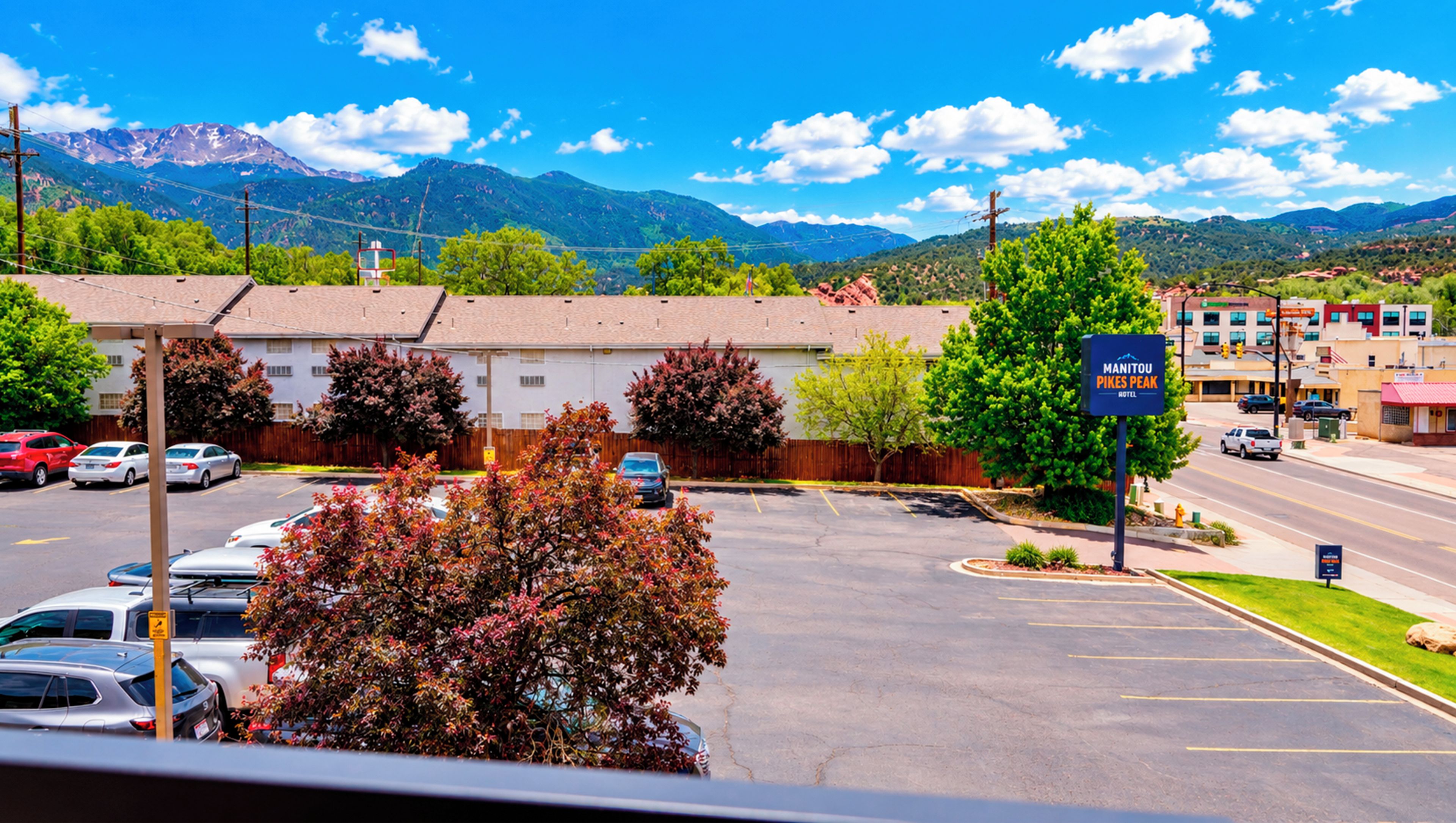 A hotel with a parking lot, a sign for Manitou Pines Peak Hotel, and a view of mountains in the background.