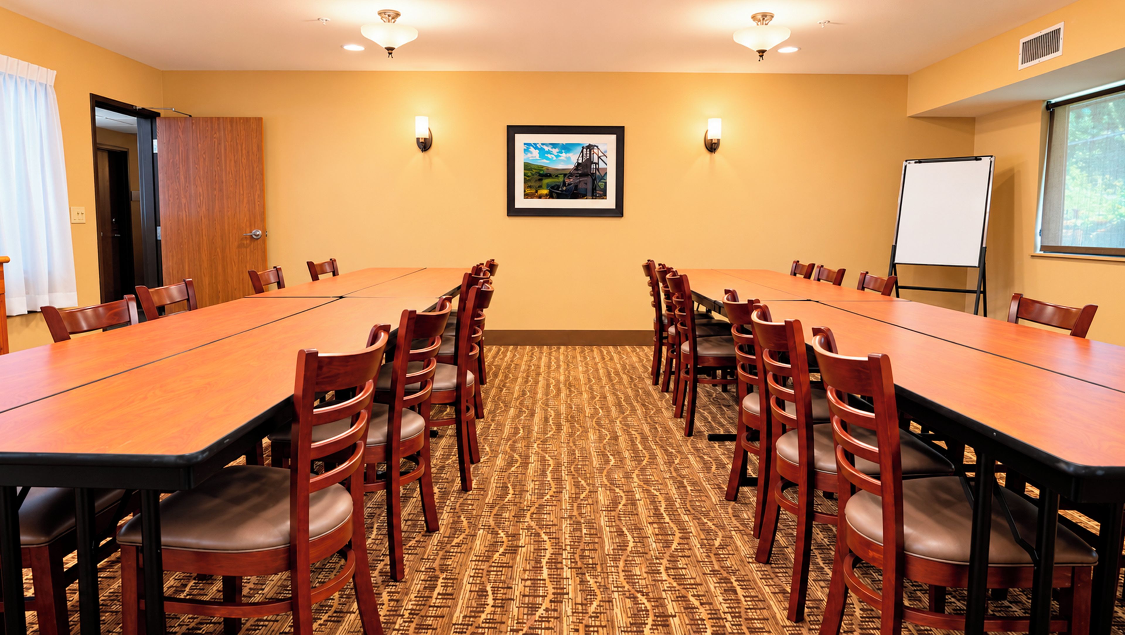 A conference room with a long table, chairs, a whiteboard, and a framed picture on the wall.