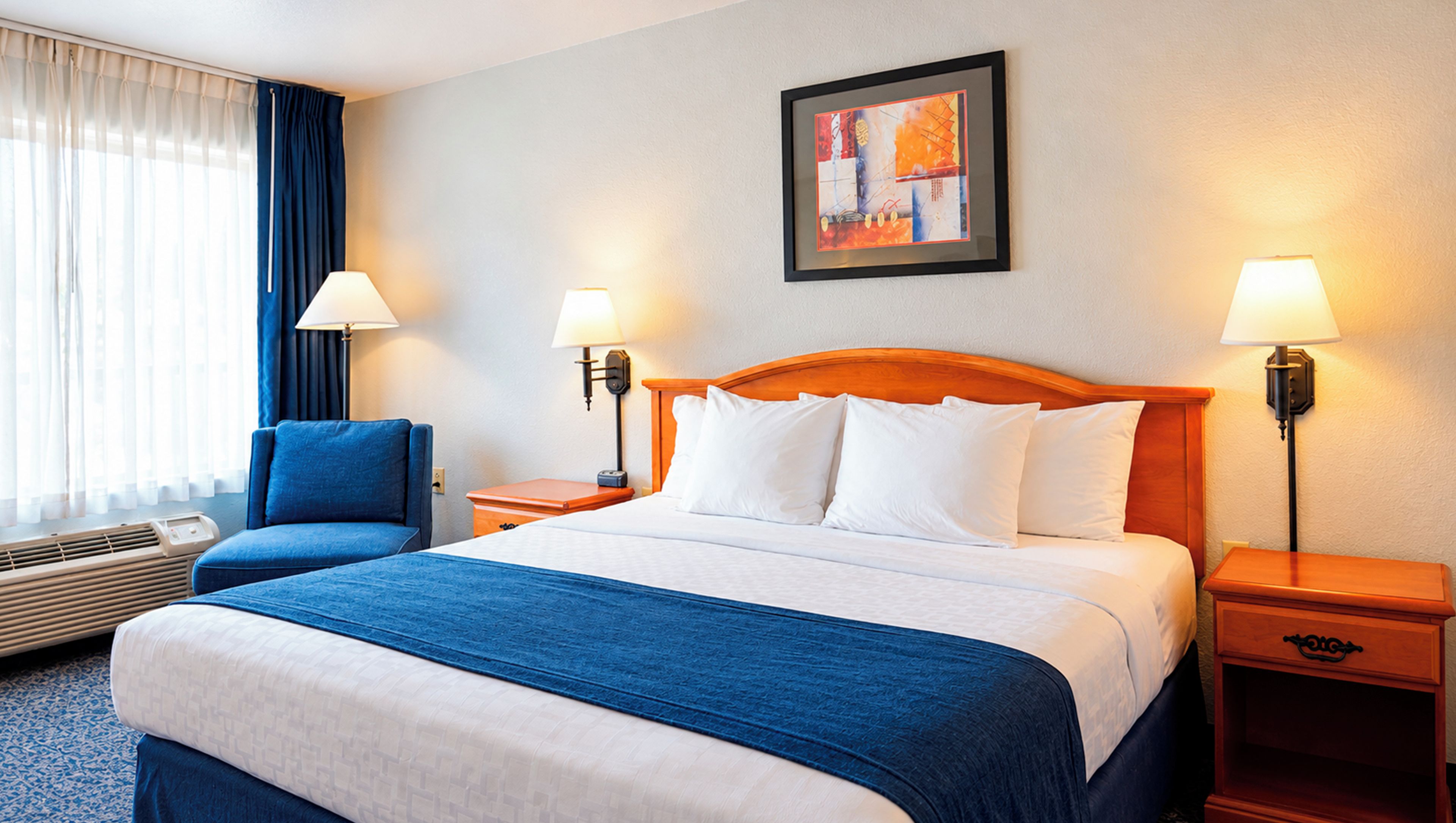 A hotel room with a bed, two bedside lamps, a chair, and a window with curtains.
