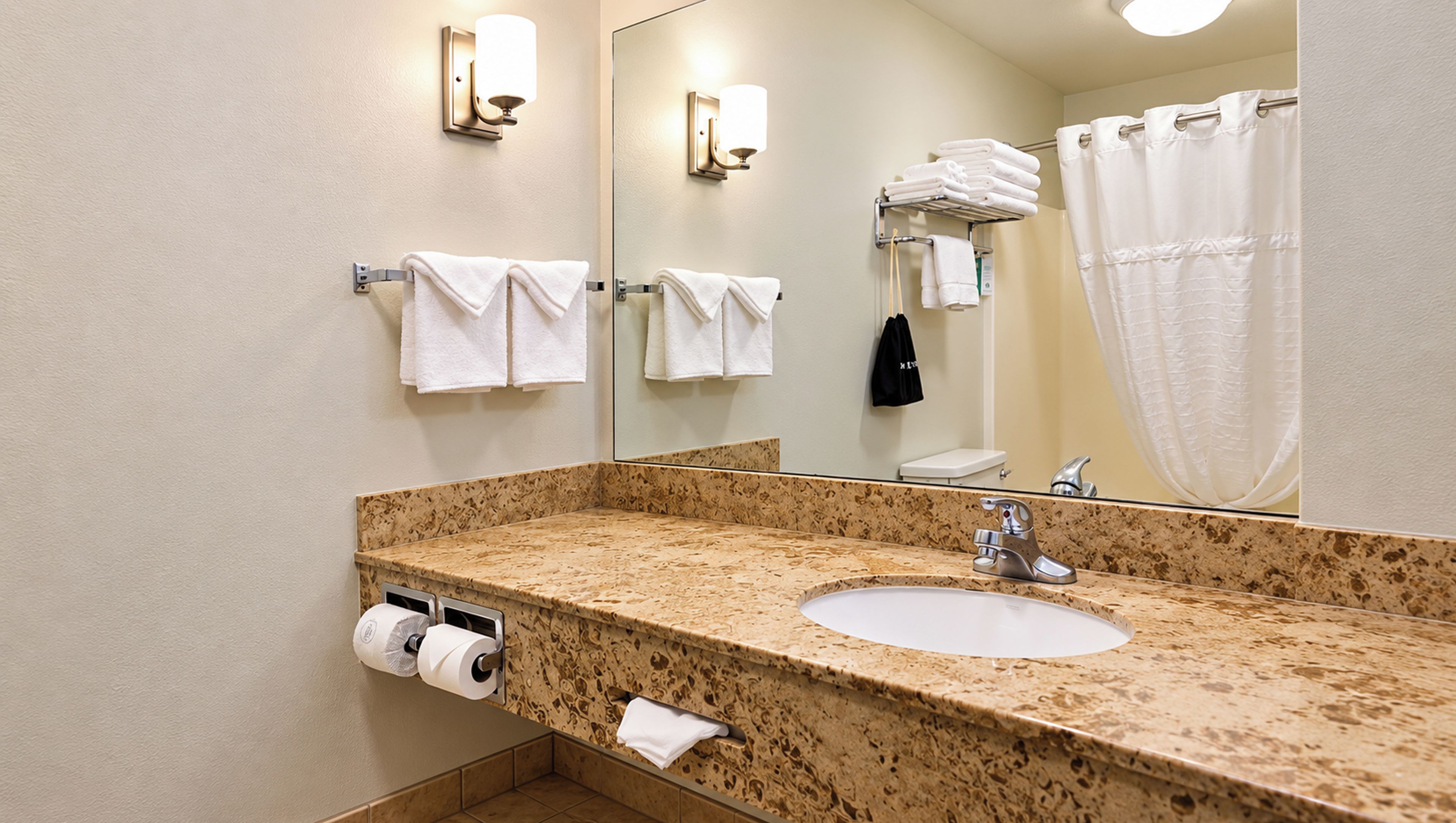 Un baño con lavamanos, espejo, toallero y retrete.