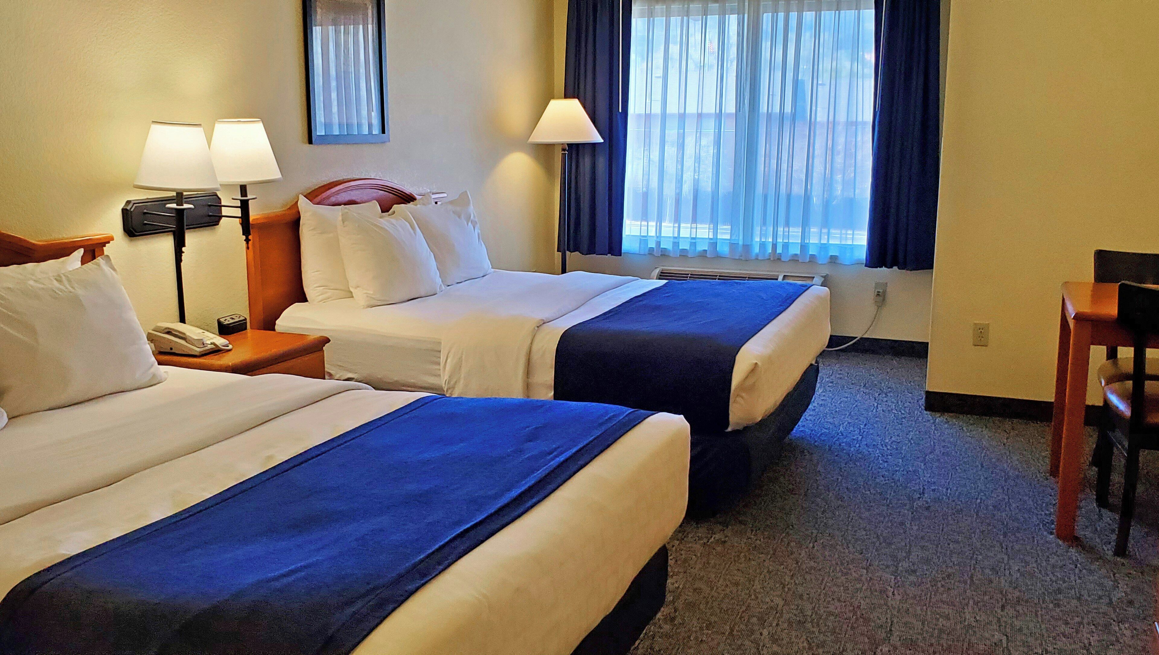 A hotel room with two beds, a desk, a chair, a telephone, and a window with curtains.