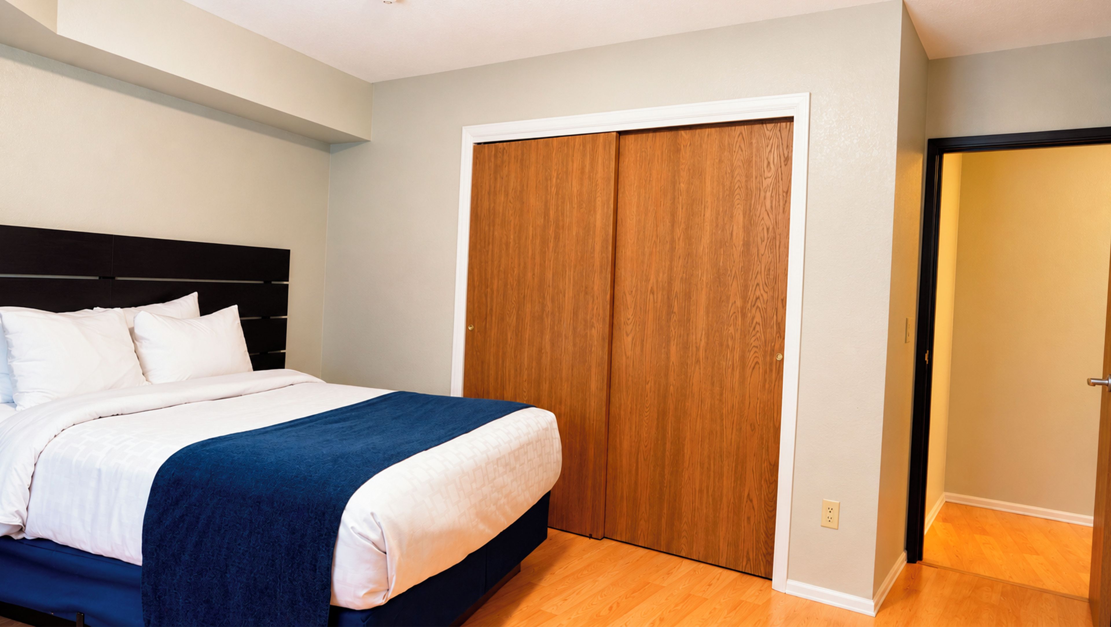 Un dormitorio con una cama, un armario de madera y una puerta que da a otra habitación.
