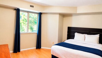 A bedroom with a bed, a window with curtains, and a wooden floor.