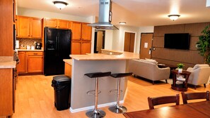 A modern kitchen with wooden cabinets, a black refrigerator, and a bar area with stools. - Manitou Pikes Peak Hotel (Manitou Springs)