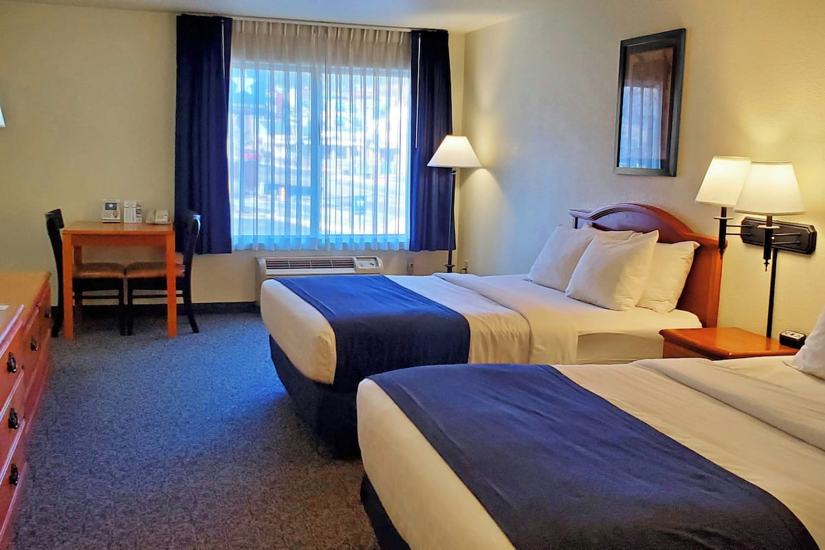 A hotel room with two beds, a desk, a chair, a television, and a window with curtains.