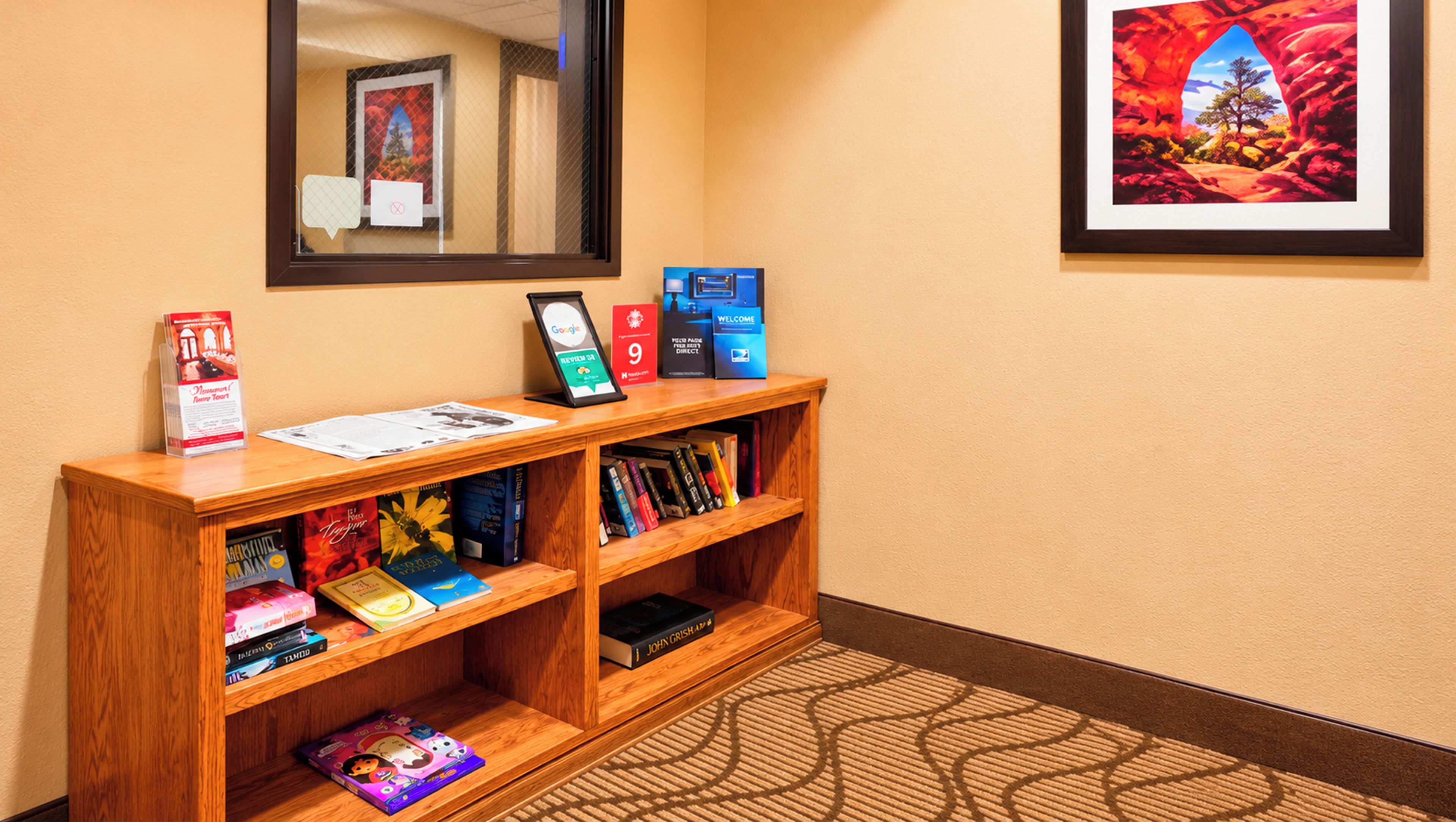 A reception desk with a mirror above it, a framed welcome sign, and a bookshelf with various books and a framed picture.