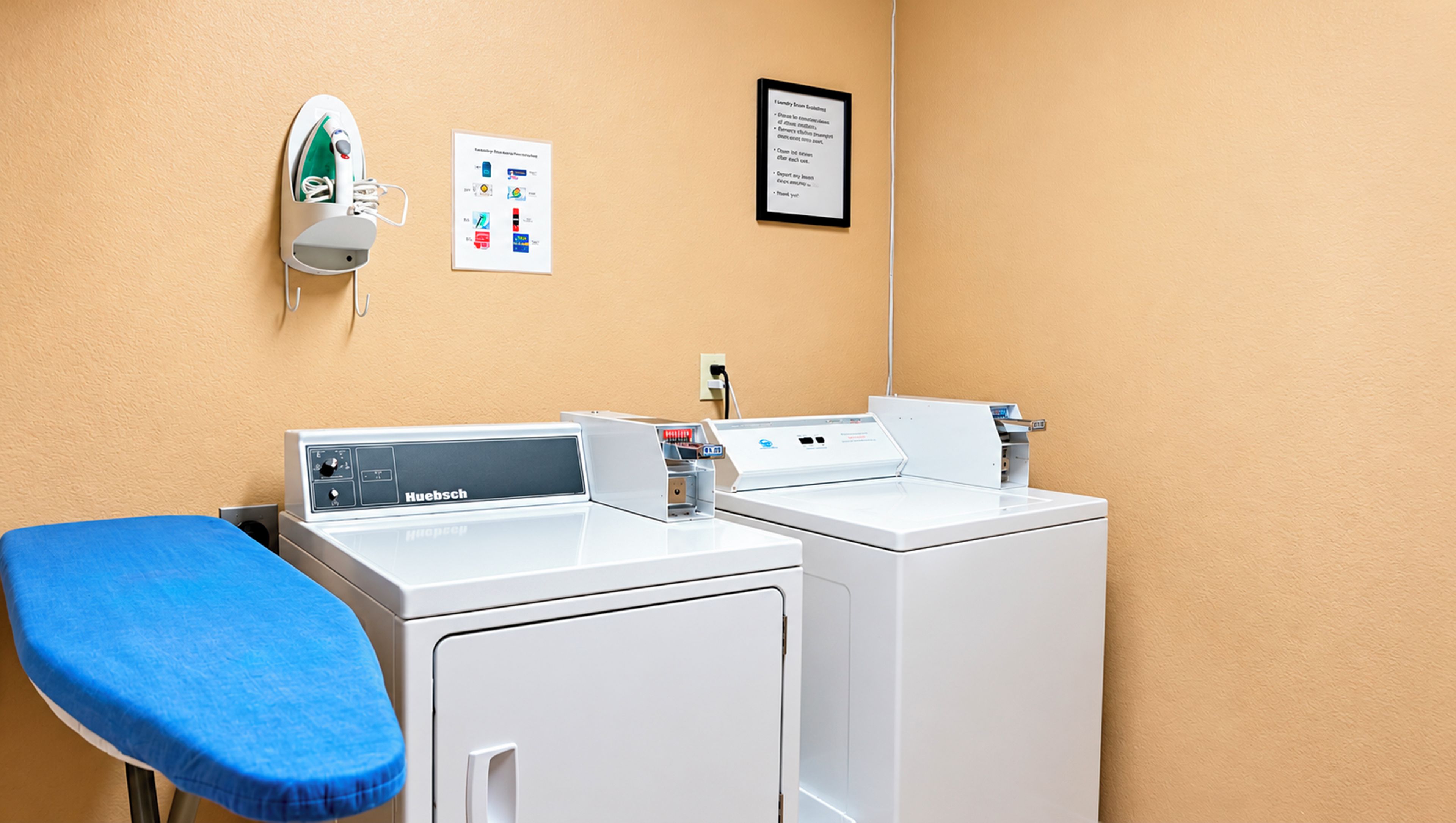 A laundry area with two white washing machines, a blue ironing board, and a wall-mounted iron.