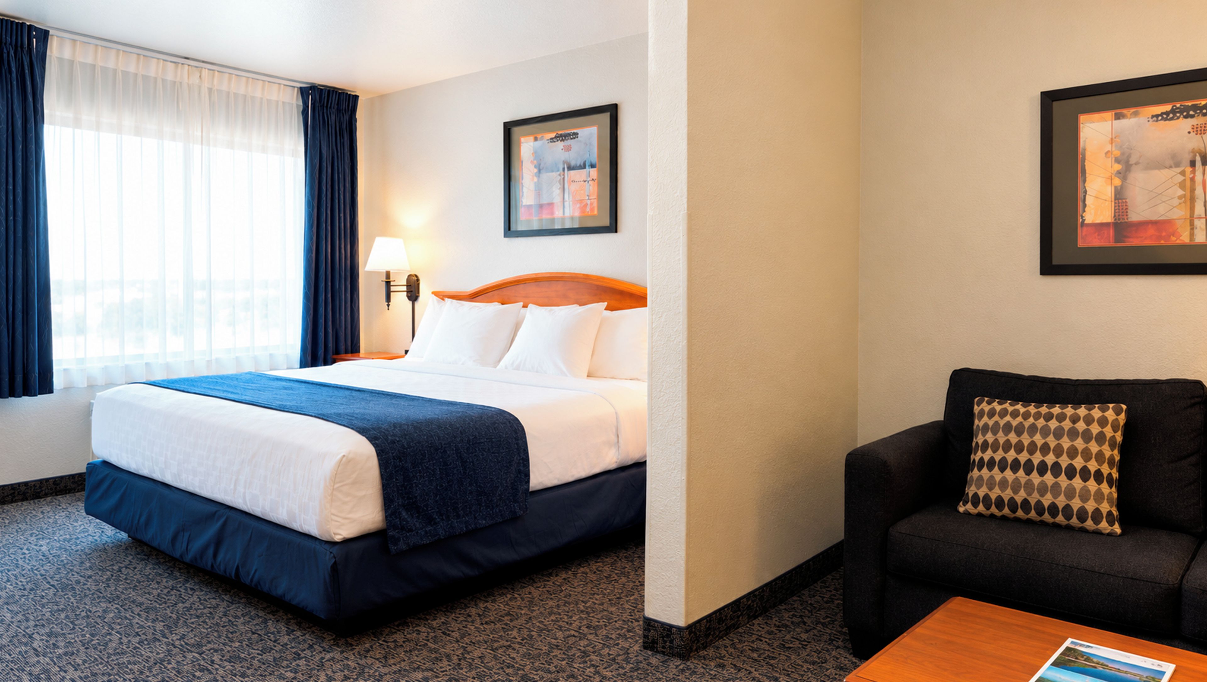 A hotel room with a bed, a sofa, a lamp, and two framed pictures on the wall.