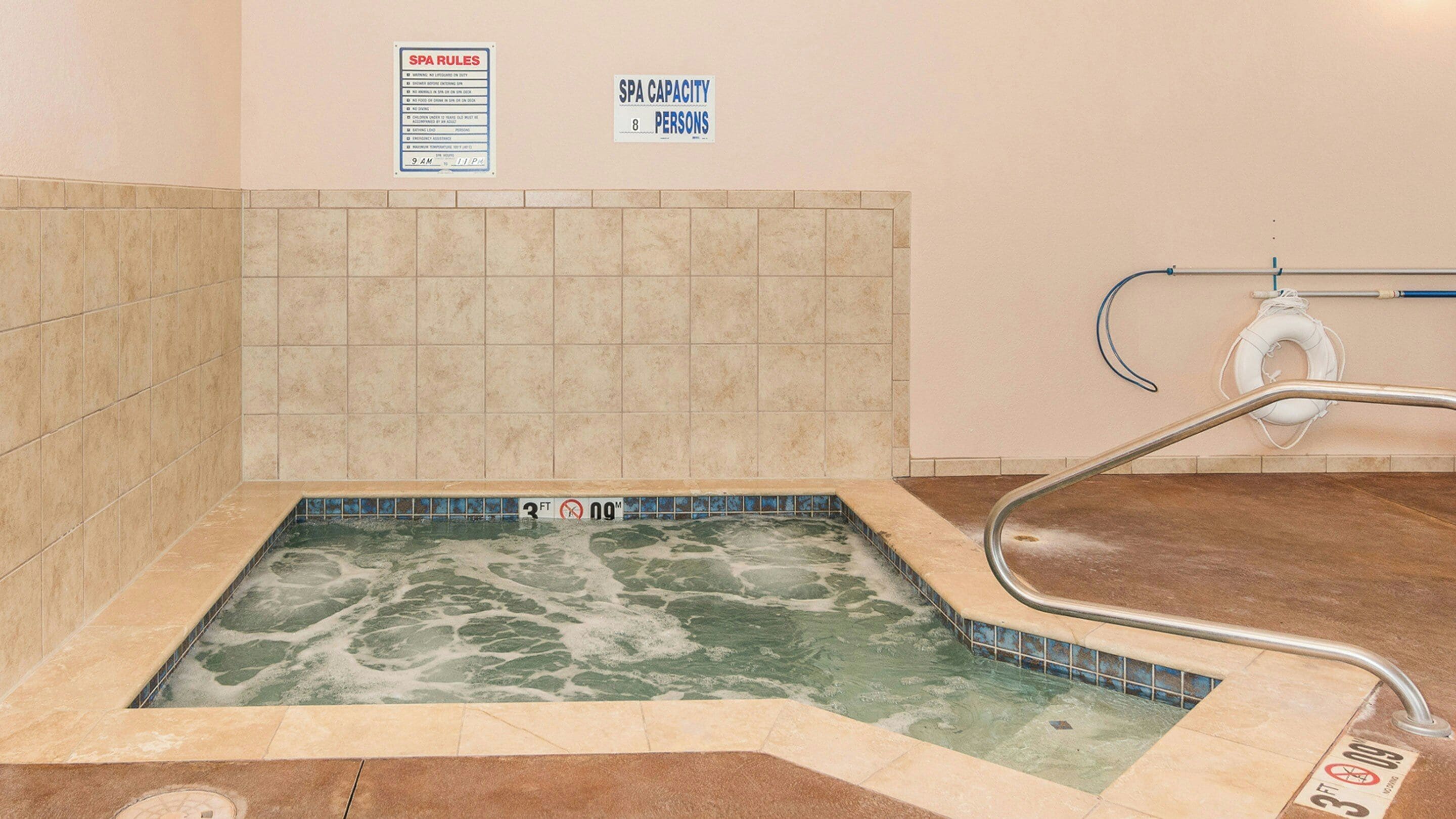 A spa with a tiled wall, a sign indicating a capacity of 8 persons, and a no swimming sign.