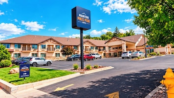 A hotel with a sign indicating the name 'Manitou Pikes Peak Hotel.' There are multiple cars parked in front, a clear sky, and a fire hydrant visible.