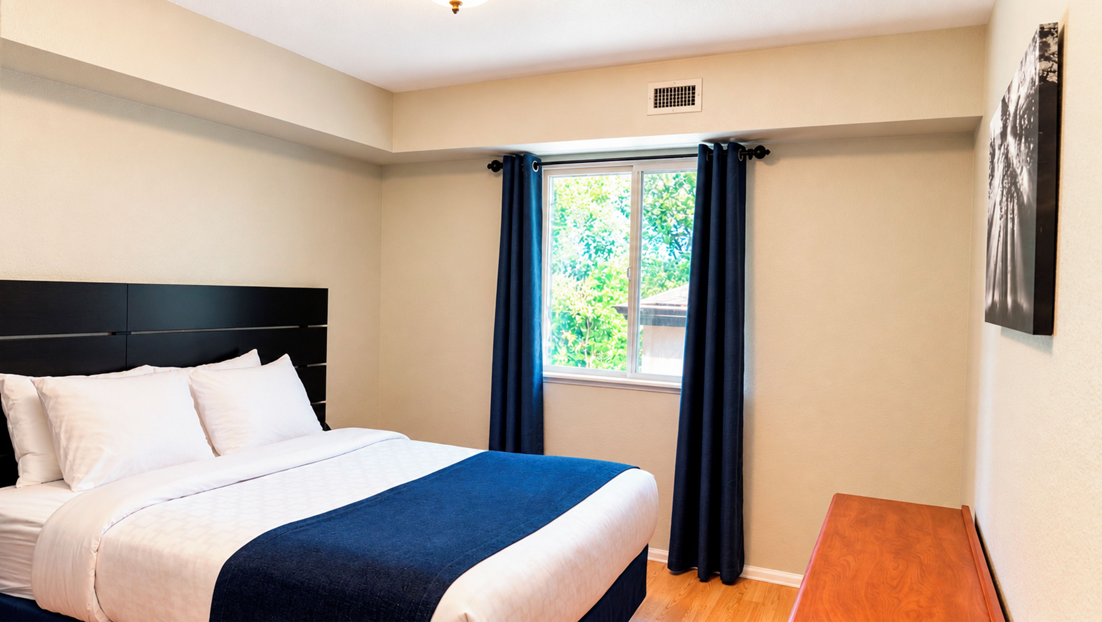 Quarto com cama, janela com cortinas, quadro na parede e mesa de cabeceira de madeira.