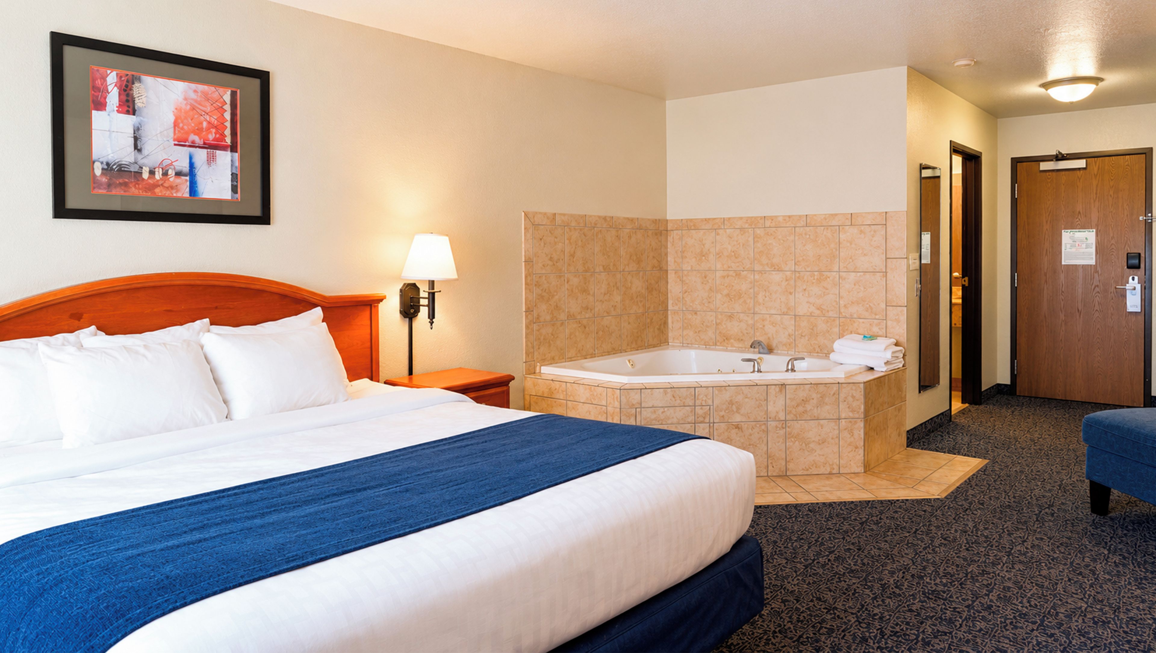 Una habitación de hotel con cama, baño con bañera y una pequeña zona de estar.