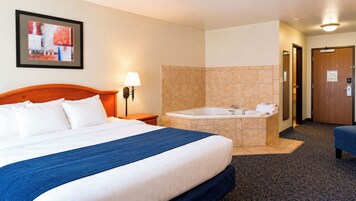 Una habitación de hotel con cama, baño con bañera y una pequeña zona de estar.