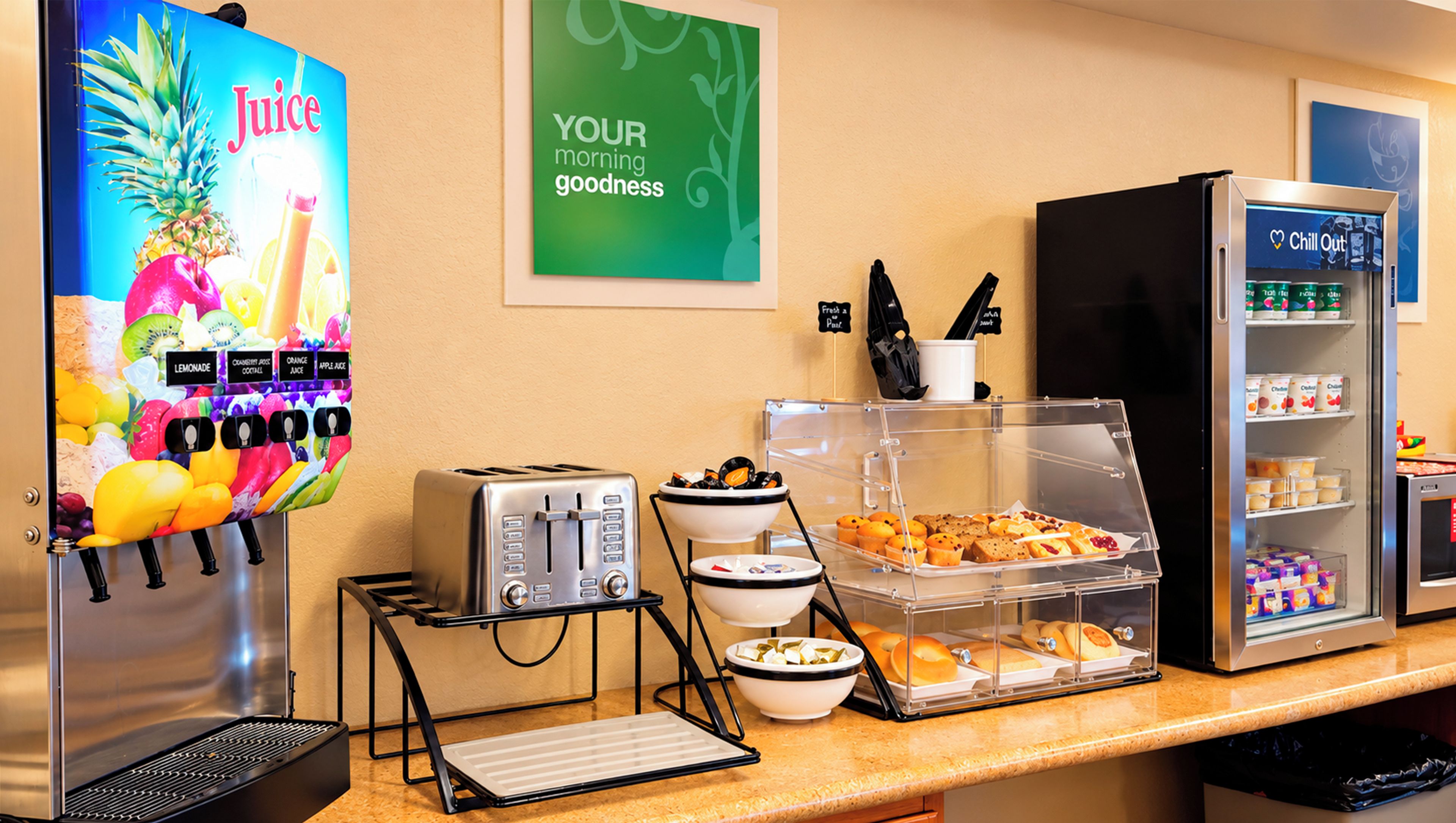 Una barra de desayuno con dispensador de zumo, tostadora y un refrigerador lleno de bebidas.