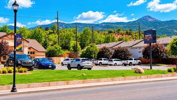 Un hotel con un cartel que indica 'MANTOU PIKES PEAK HOTEL', un estacionamiento con varios vehículos y una cadena montañosa al fondo.