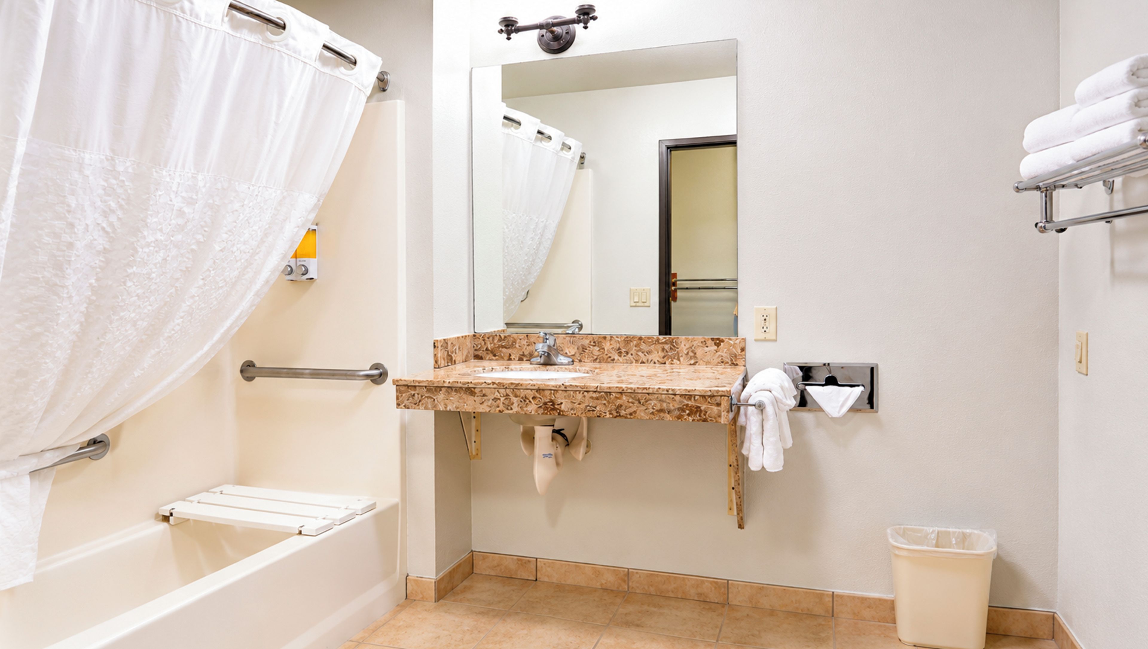 A bathroom with a bathtub, a sink with a mirror, a towel rack, and a trash bin.