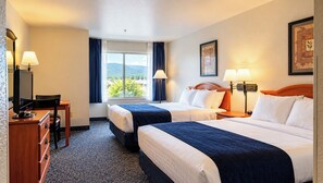 A hotel room with two beds, a desk with a computer, a chair, a window with curtains, and a lamp. - Manitou Pikes Peak Hotel (Manitou Springs)
