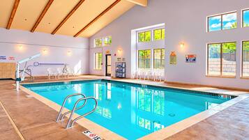 An indoor swimming pool with clear water, a diving board, and multiple windows.