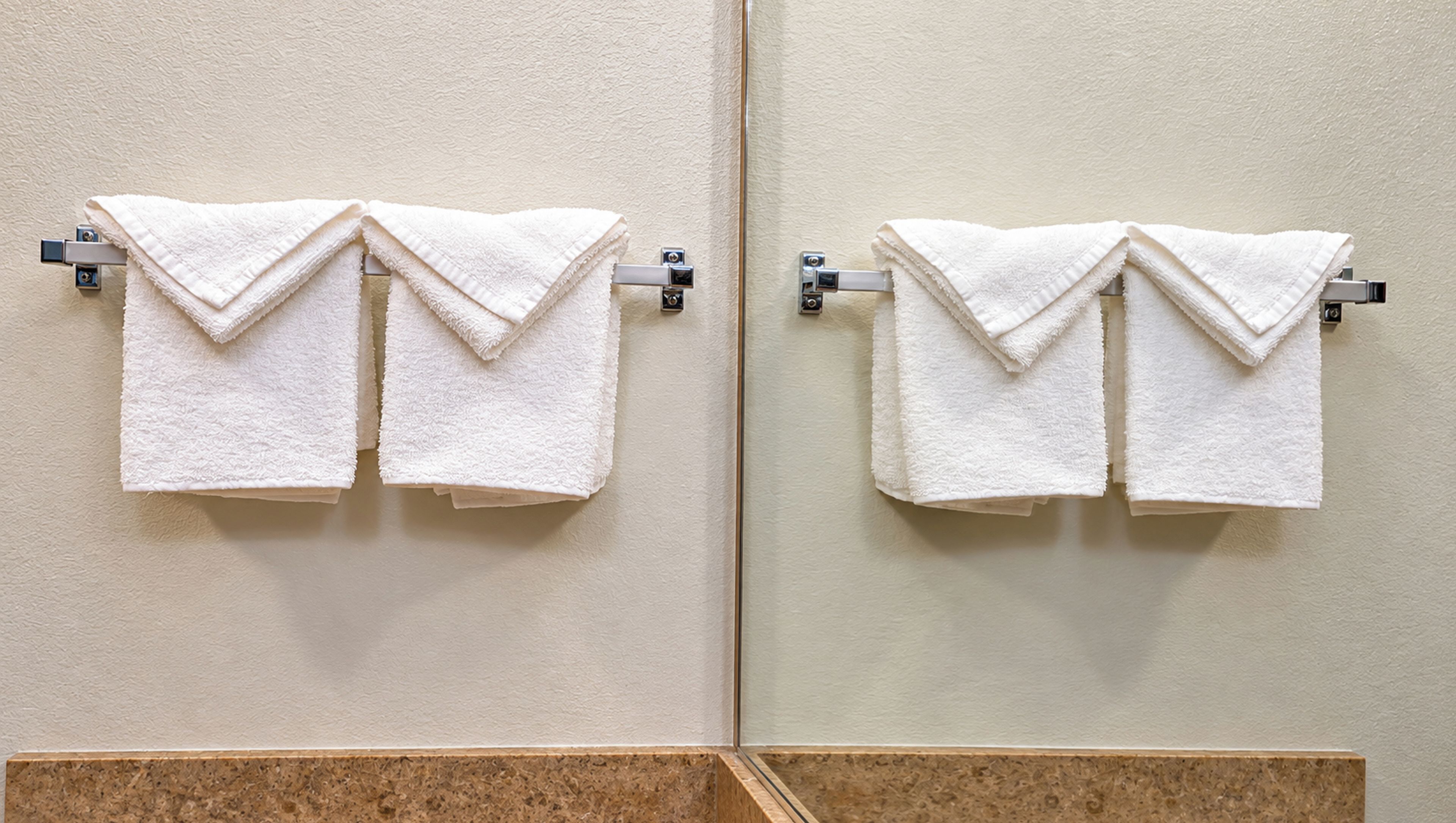 Ein Badezimmer mit zwei weißen Handtüchern an Handtuchhaltern, einem Spiegel und einer strukturierten Wand.