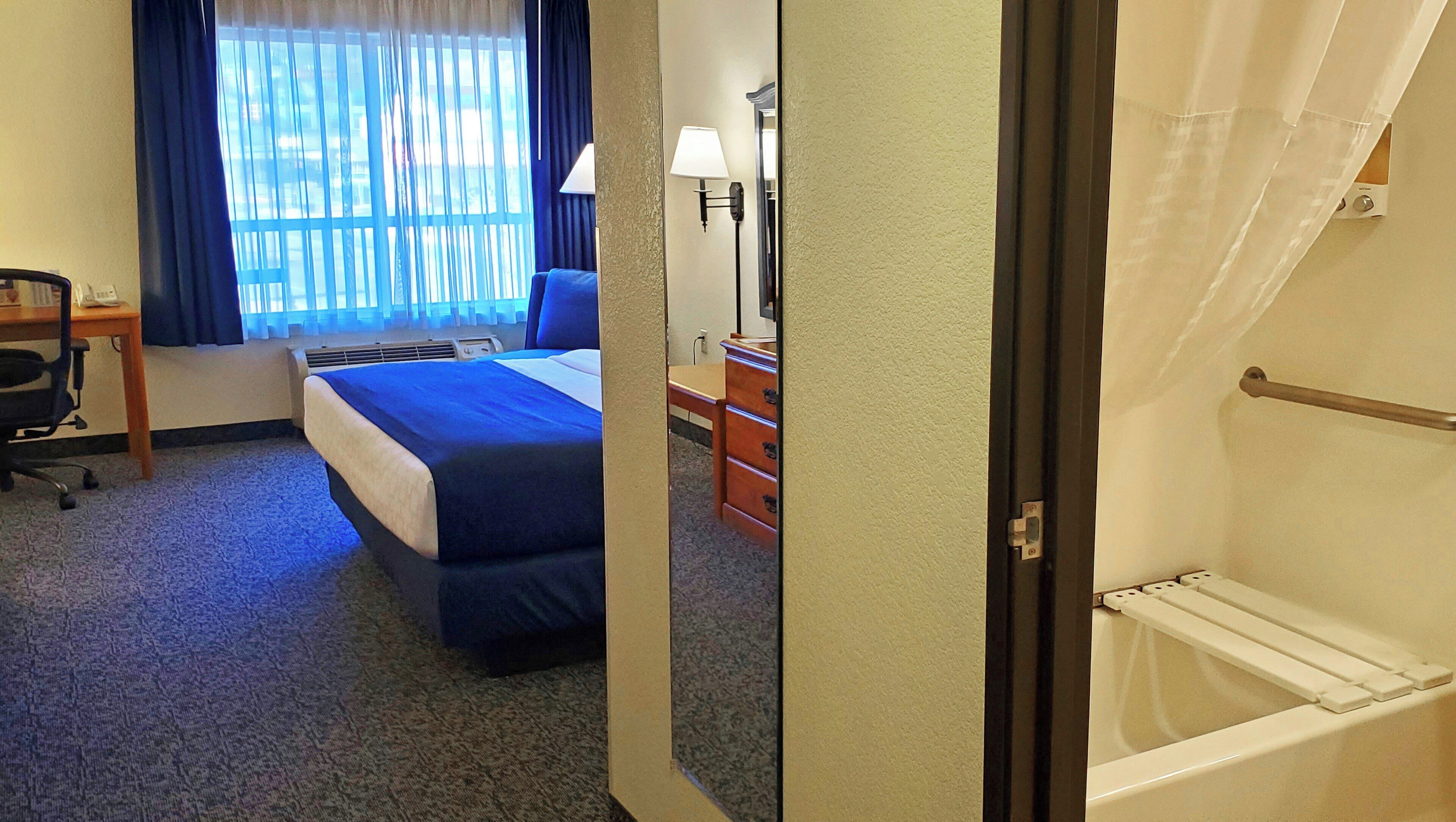 A hotel room with a bed, desk, chair, dresser, and a view of the outdoors through the window.