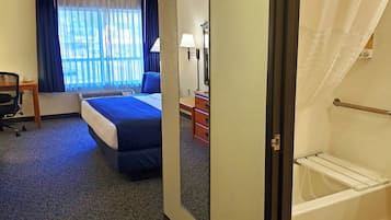 A hotel room with a bed, desk, chair, dresser, and a view of the outdoors through the window.