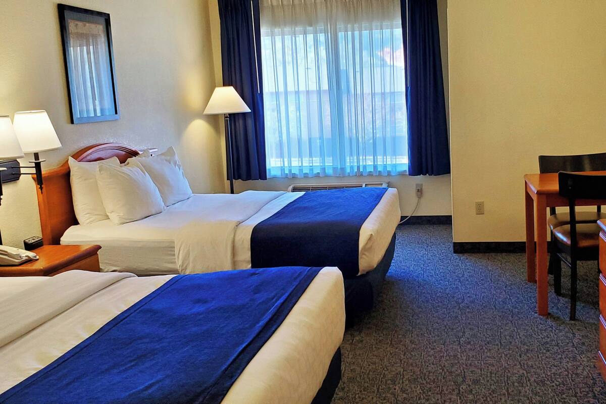 A hotel room with two beds, a desk, a chair, a TV, and a window with curtains.