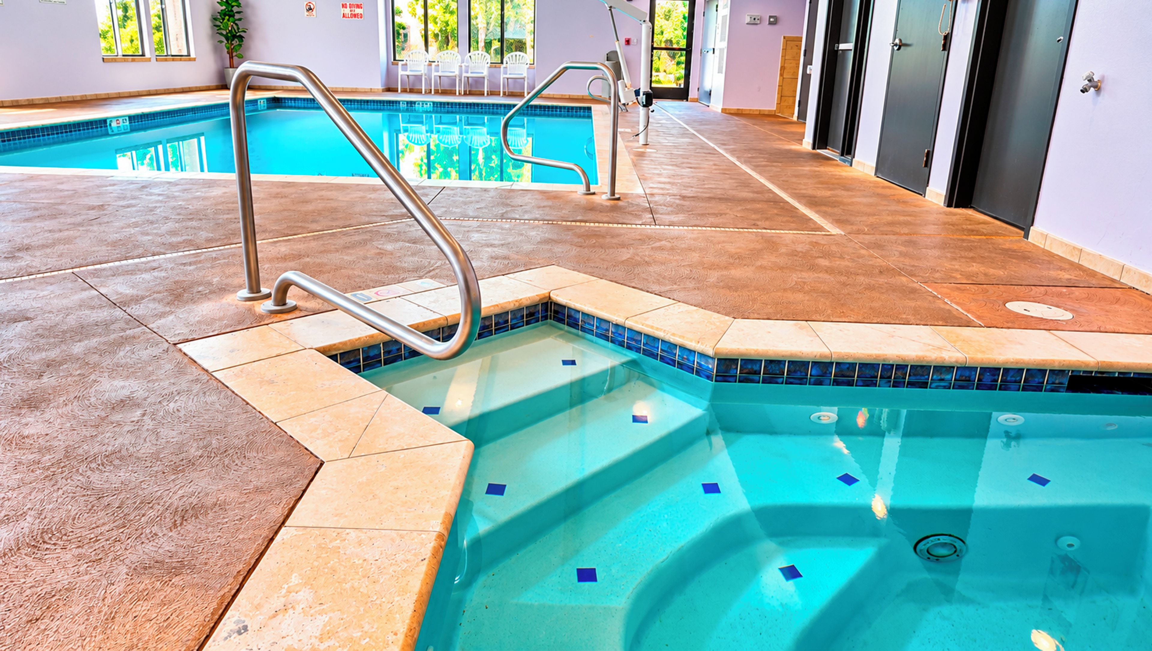 An indoor swimming pool with a tiled edge, a metal ladder, and a tiled floor.