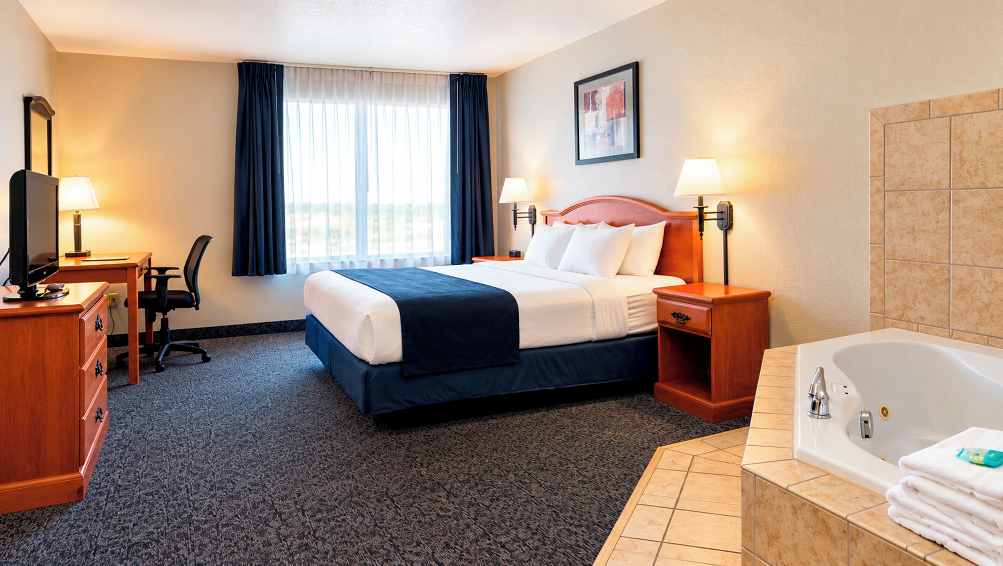 Een hotelkamer met een bed, een bureau, een stoel, een televisie, een raam met gordijnen, een schilderij aan de muur, een nachtkastje met een lamp en een badkuip met handdoeken.